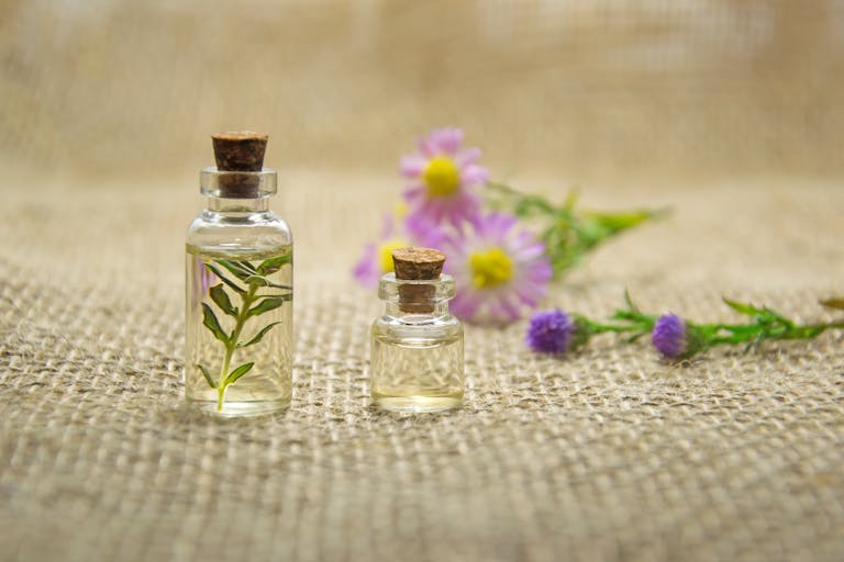 Glass bottles with essential oils and fresh flowers on burlap fabric creating a natural aroma.